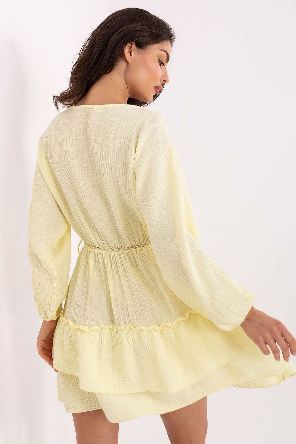 Woman wearing a light yellow dress with long sleeves on a white background