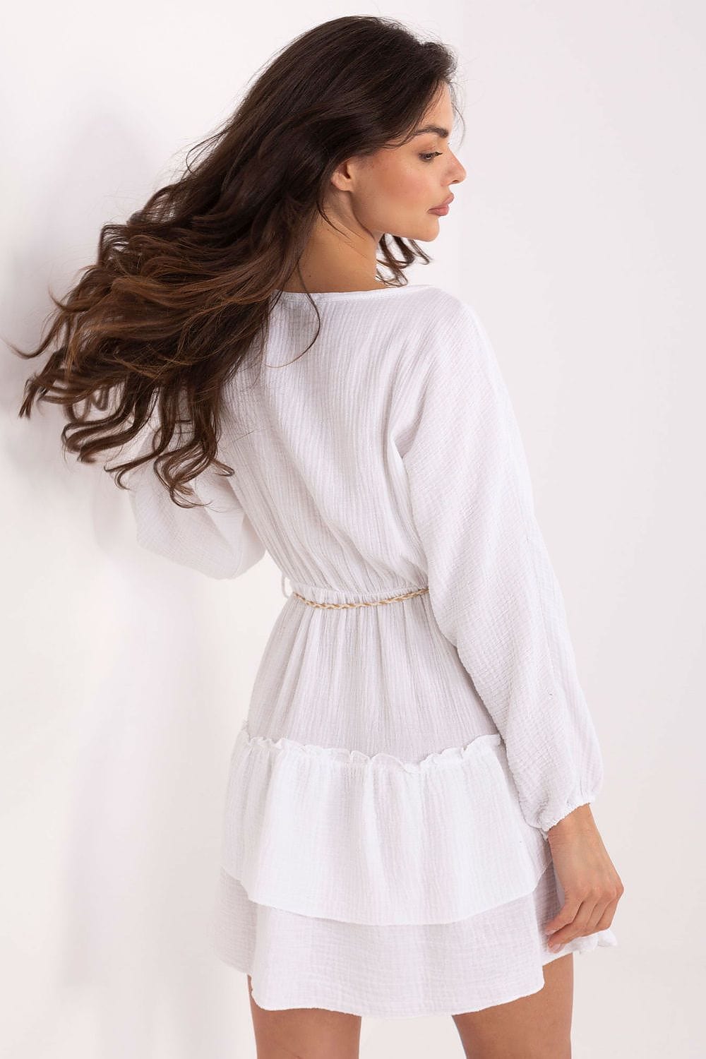 Woman wearing a white dress with long sleeves on a plain background