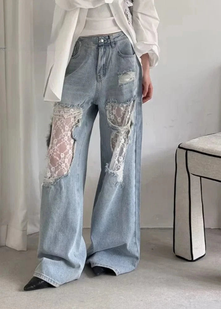 Person wearing patchwork jeans with lace inserts in a minimal indoor setting.
