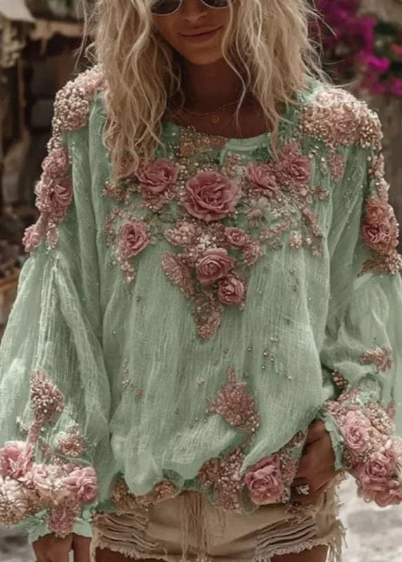 Woman wearing a light green blouse with floral embellishments in an outdoor setting.