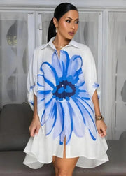 Woman wearing a white dress with a large blue flower design in a room.