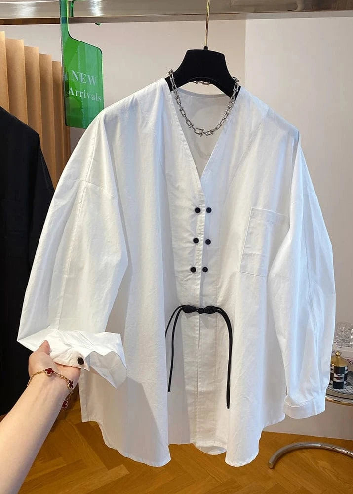 White blouse with black buttons and a belt on a hanger, with a blurred background.