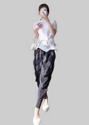 Person taking a mirror selfie wearing a white top and dark pants in a room with wooden floor and white walls.