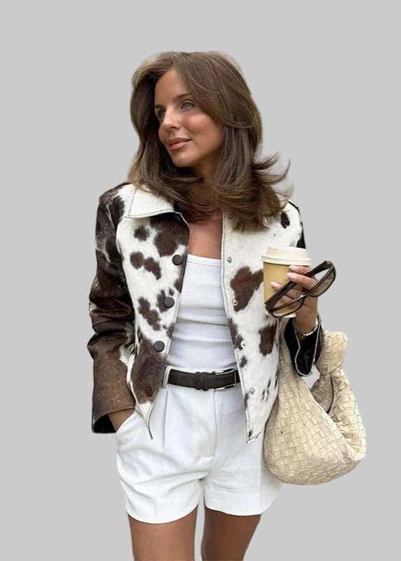 Woman in a cow print jacket and white shorts standing on a street.