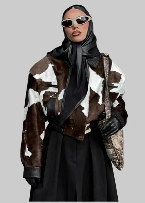 Person wearing a cow print coat with a black outfit and sunglasses in an urban setting