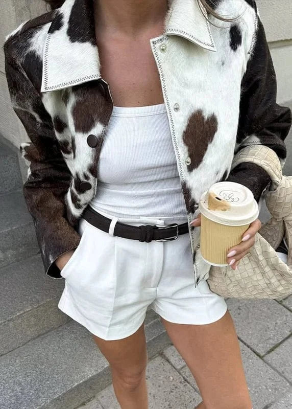 Person wearing a cow print jacket, white top, and shorts, holding a coffee cup and bag.