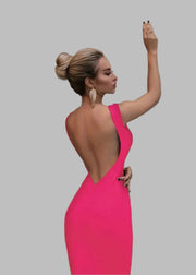 Woman in a bright pink dress with a low back, standing against a beige wall.