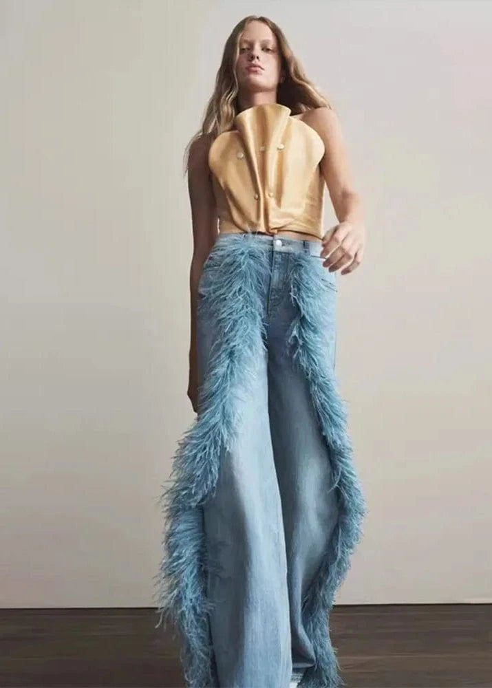 Woman wearing a gold top and blue feathered skirt against a plain background