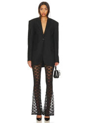 Woman wearing a black blazer and lace pants on a white background