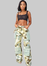 Woman wearing a black crop top and camouflage pants standing on a sidewalk.