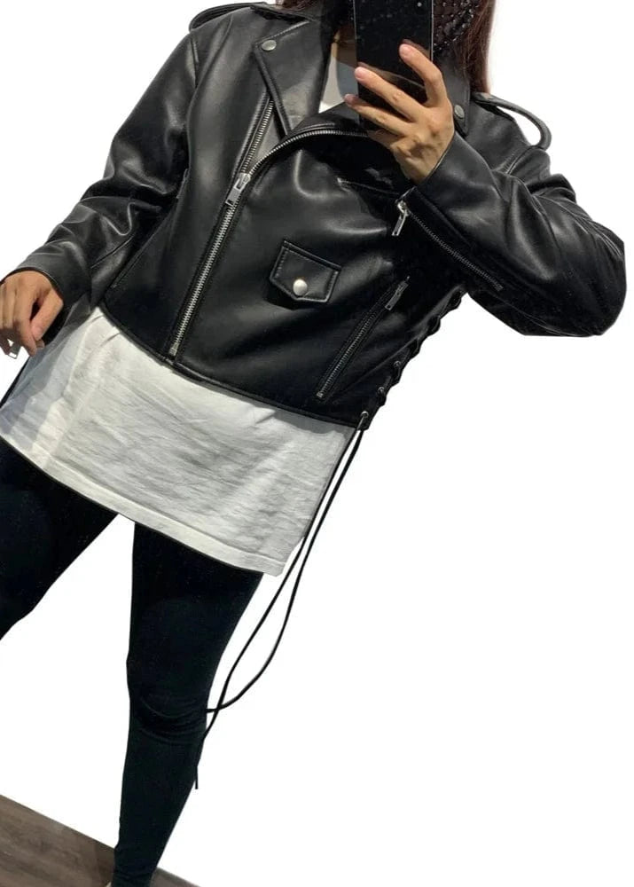 Person wearing a black leather jacket and black leggings with white stripes, standing on a wooden floor.