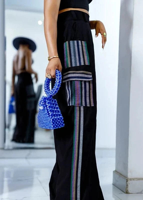 Person wearing a black outfit with colorful stripes holding a blue handbag.