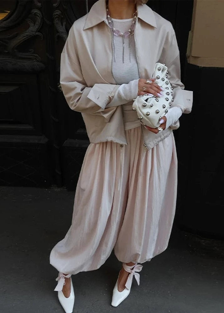 Person wearing a beige trench coat and pants holding a white studded handbag.