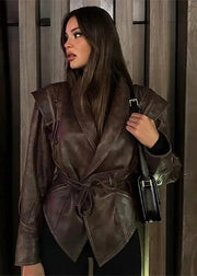Woman wearing a brown leather jacket holding a black handbag indoors.