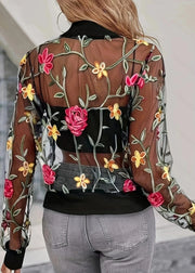 Person wearing a sheer jacket with floral embroidery in a blurred indoor setting