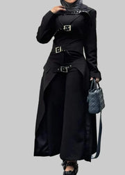 Person wearing a black outfit with a belt and holding a handbag, standing outdoors.