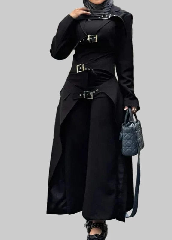 Person wearing a black outfit with a belt and holding a handbag, standing outdoors.