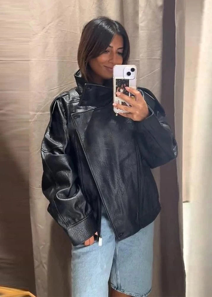 Person wearing a black leather jacket and light blue jeans taking a mirror selfie.