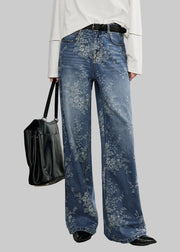 Person wearing blue floral jeans holding a black bag against a white background