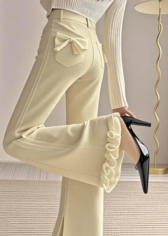 Beige pants with ruffled cuffs worn by a person, standing in a room with a lamp.