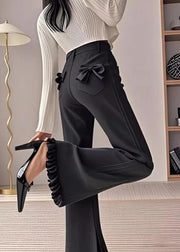 Person wearing black pants with a bow detail and high heels in an indoor setting.