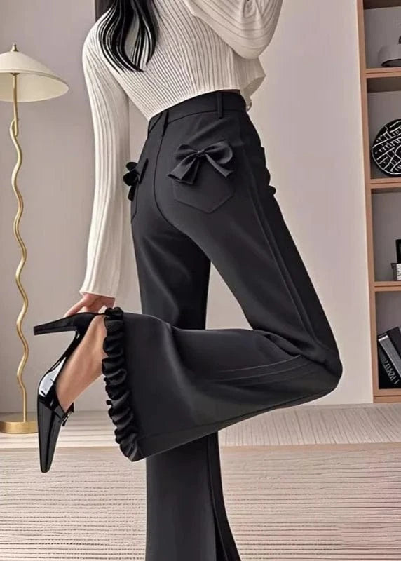 Person wearing black pants with a bow detail and high heels in an indoor setting.