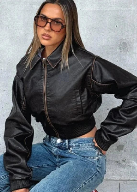 Woman wearing a black leather jacket and blue jeans against a gray concrete wall.