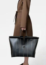 Person holding a black leather handbag with a plain background