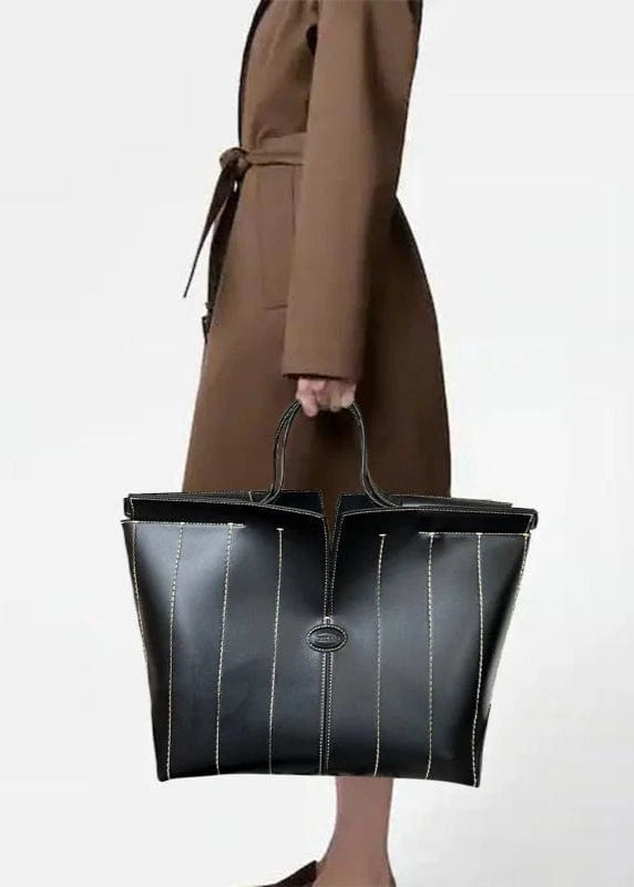 Person holding a black leather handbag with a plain background