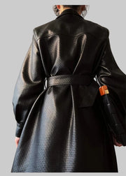 Person wearing a black textured coat with a belt, holding an umbrella indoors.