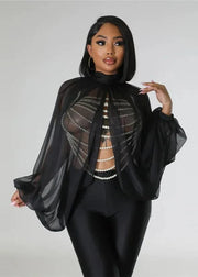 Woman wearing a black outfit with sheer overlay and pearl details on a plain background