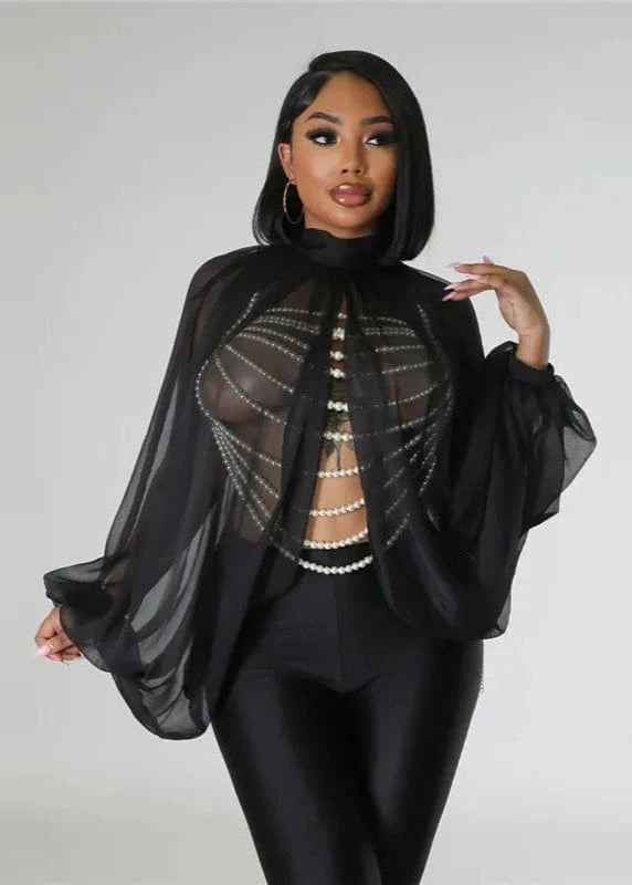 Woman wearing a black outfit with sheer overlay and pearl details on a plain background