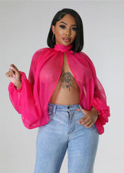 Woman wearing a bright pink sheer blouse over a black top with blue jeans on a plain background