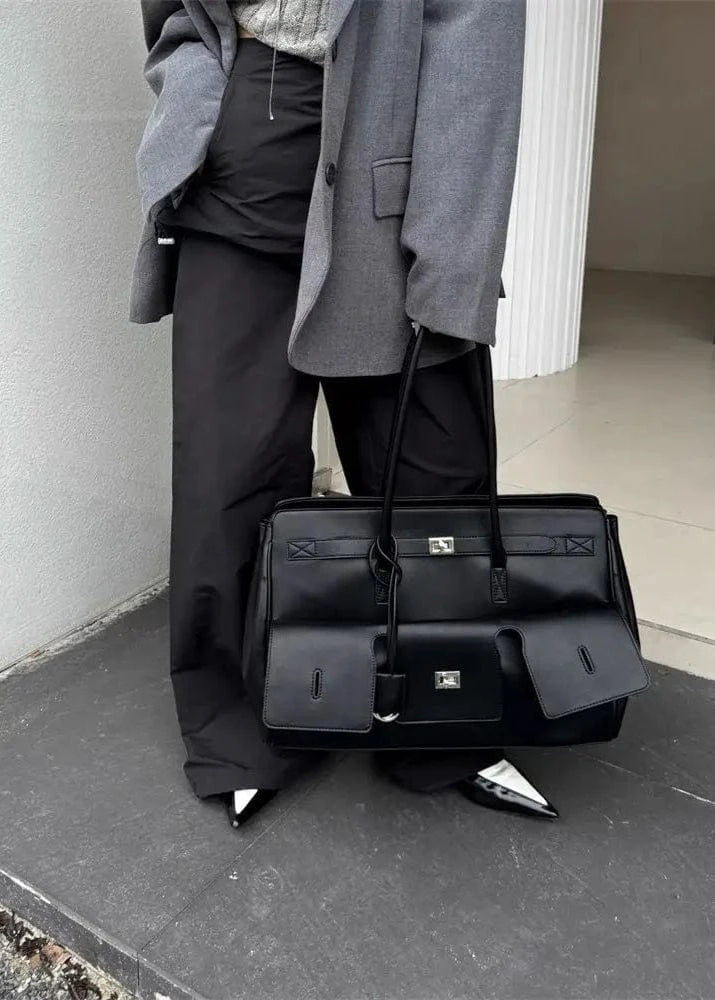 Person holding a black leather bag against a neutral background