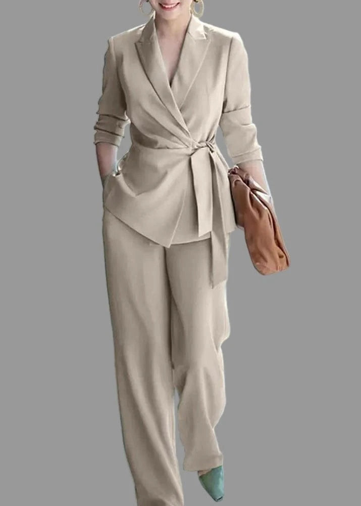 Woman wearing a beige suit with a brown handbag in an indoor setting
