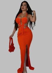 Woman wearing an orange dress with a high slit, holding a matching handbag, in a room with a white couch.