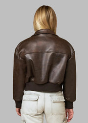 Person wearing a brown leather jacket against a beige curtain background