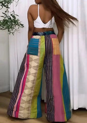 Person wearing colorful patterned pants with a white top against a white curtain background