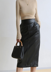Person wearing a beige long-sleeve top and black leather skirt, holding a black handbag against a plain background.