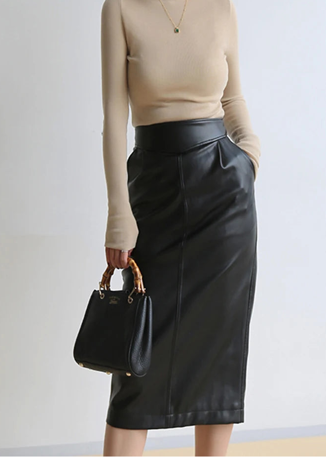 Person wearing a beige long-sleeve top and black leather skirt, holding a black handbag against a plain background.