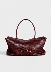 A burgundy crocodile-embossed leather handbag with a single top handle and gold-tone hardware, shown against a plain light gray background.