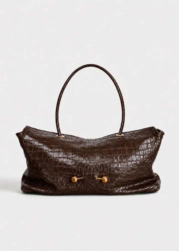 A dark brown crocodile-embossed leather handbag with a single top handle and gold-tone toggle hardware, shown against a light gray studio background.
