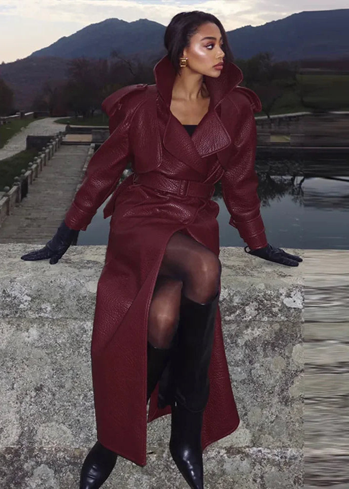 Woman in a long burgundy coat standing outdoors with mountains in the background