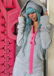 Person wearing a gray hoodie with a pink zipper in front of a textured wall.