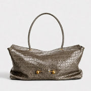 A metallic taupe crocodile-embossed leather handbag with a single top handle and gold-tone hardware, shown against a plain light gray background.