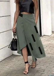 Woman wearing a green skirt with black accents and a black top, standing on a sidewalk.