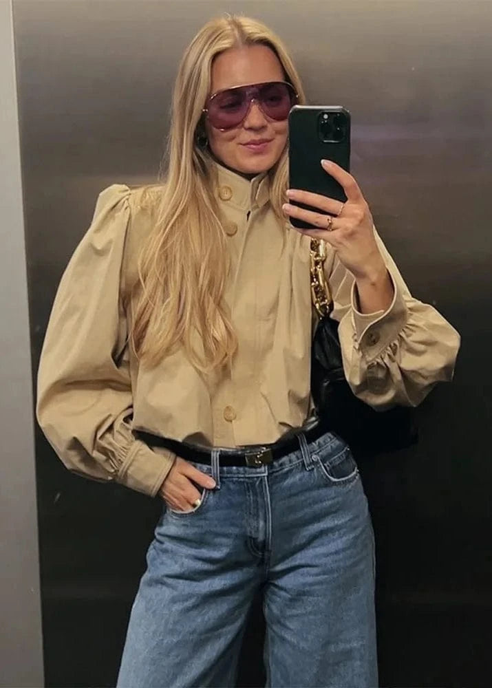 Person taking a mirror selfie wearing a beige blouse, blue jeans, and sunglasses.