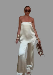 Woman in a strapless top and wide-leg pants holding sunglasses indoors.