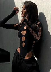 Woman wearing a black outfit with cut-out designs against a gray wall.