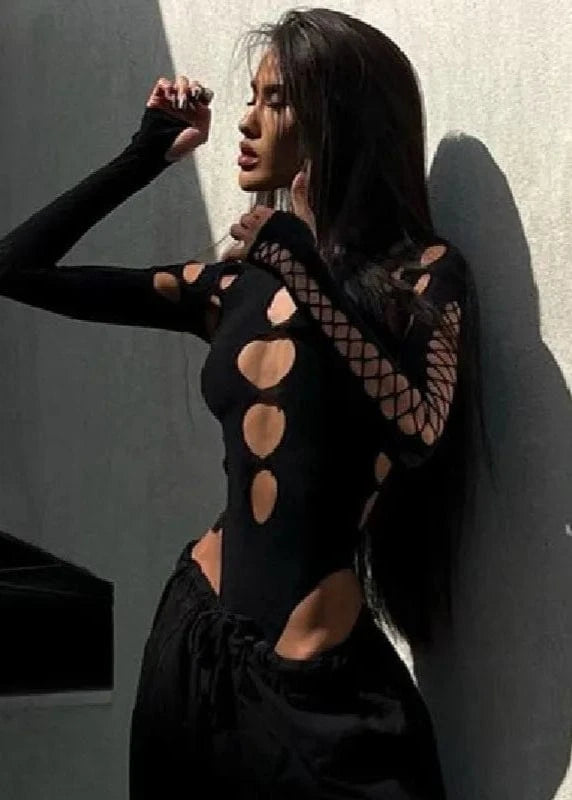Woman wearing a black outfit with cut-out designs against a gray wall.